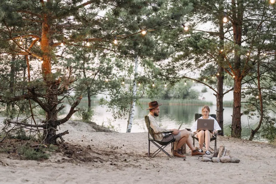 Paar mit Laptops am Seeufer eines Campingplatzes zwischen Kiefern