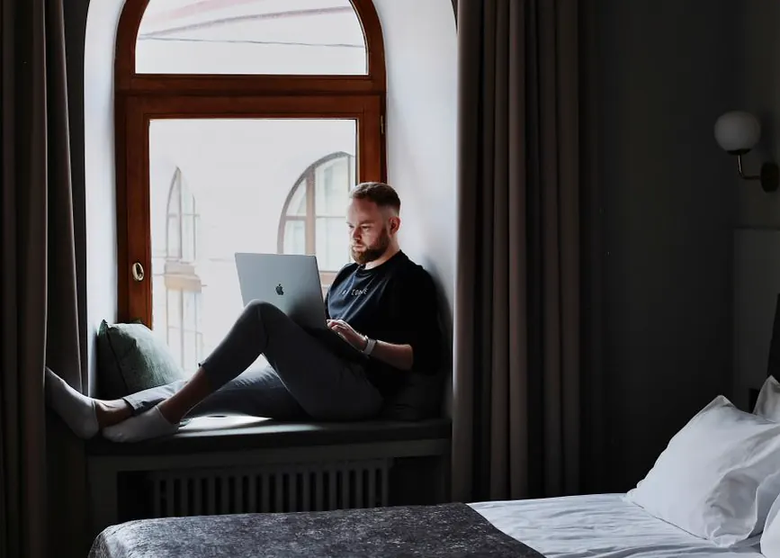Gast mit Laptop auf der Fensterbank eines Hotelzimmers