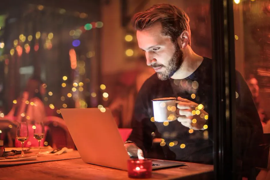 Gast mit Kaffeetasse und Laptop in einem Café am Abend