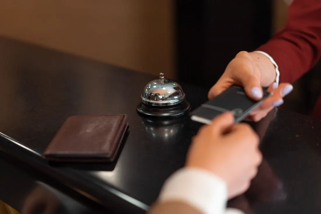 Hands at a reception desk: a card is handed across the desk, next to a bell and a wallet